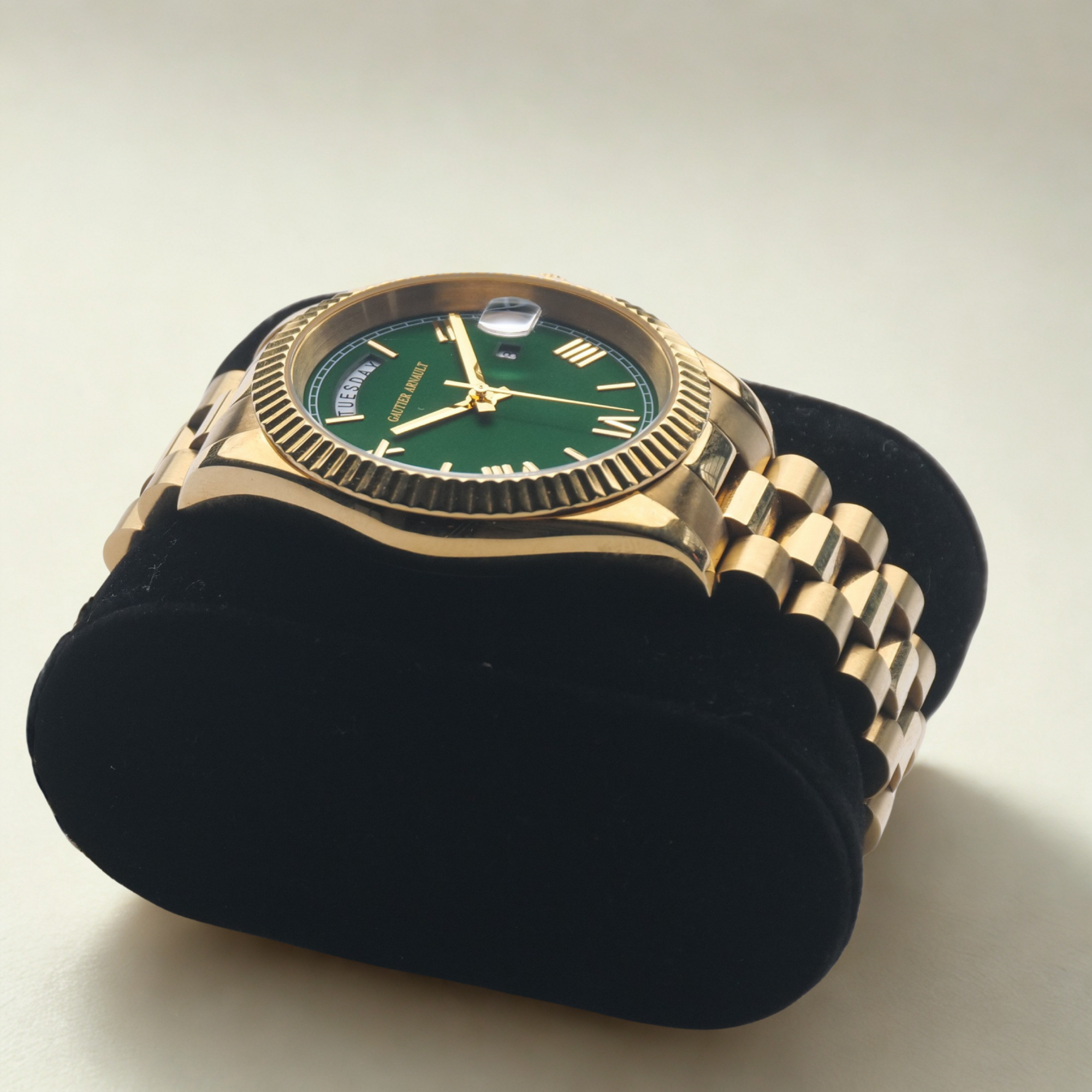 Gold watch with a green face on a black stand against a beige background